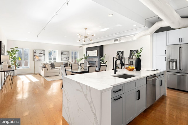 kitchen with light stone countertops, stainless steel appliances, sink, a kitchen island with sink, and gray cabinetry