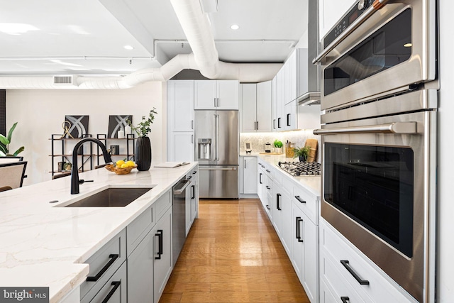 kitchen featuring sink, white cabinetry, light stone countertops, light hardwood / wood-style floors, and stainless steel appliances