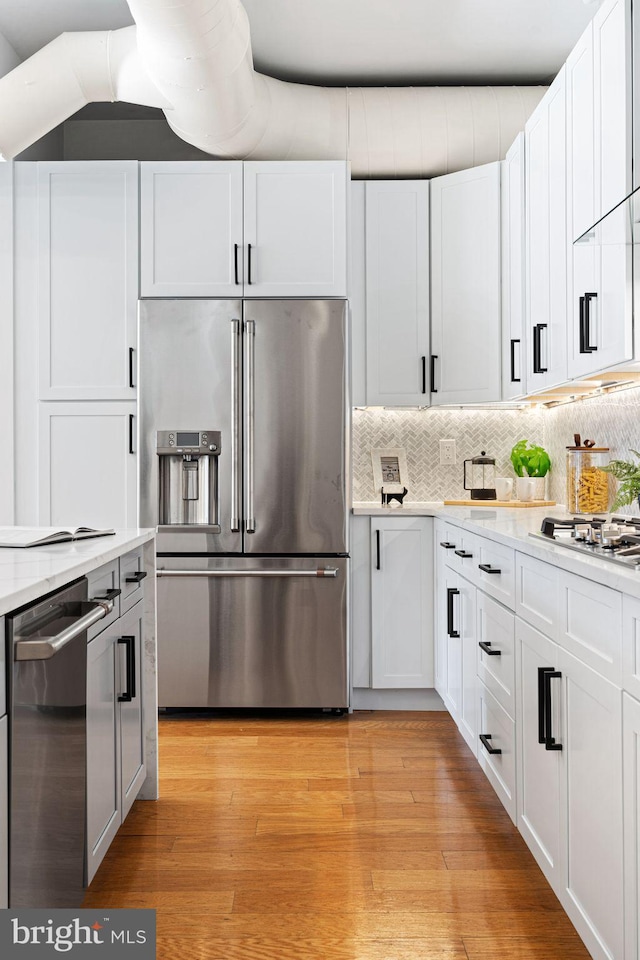 kitchen with light hardwood / wood-style floors, light stone countertops, appliances with stainless steel finishes, tasteful backsplash, and white cabinetry