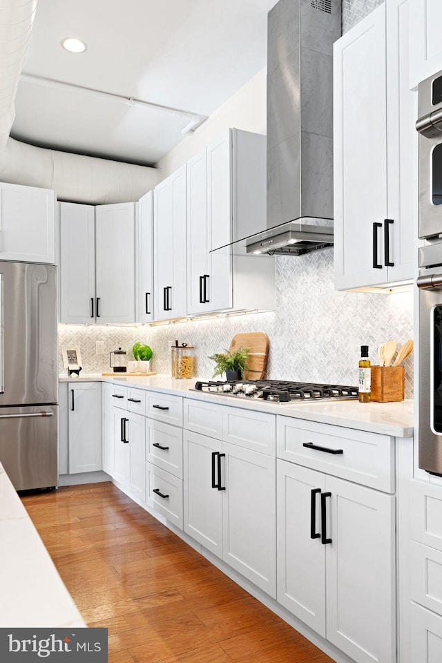 kitchen featuring white cabinetry, wall chimney range hood, and stainless steel appliances