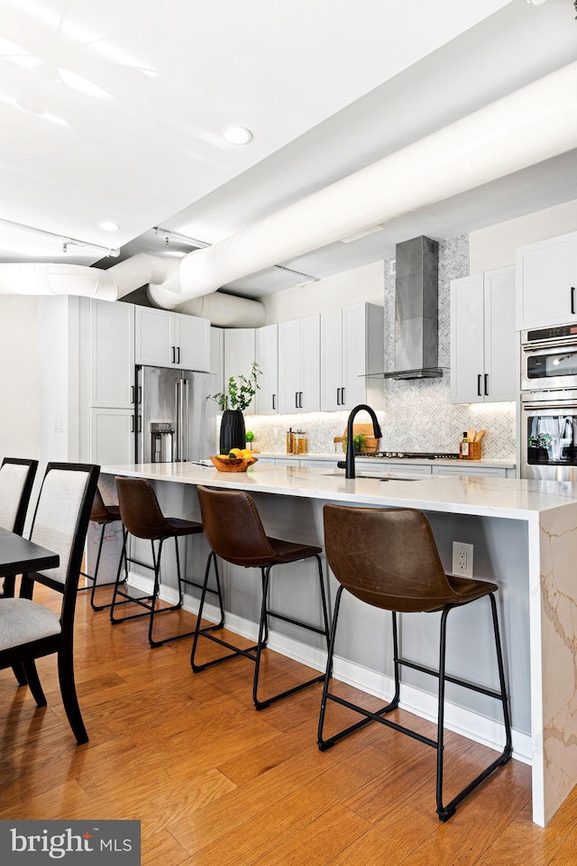 kitchen with wall chimney exhaust hood, white cabinetry, a breakfast bar, and appliances with stainless steel finishes