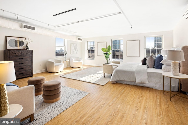 bedroom with light wood-type flooring, a wall mounted AC, and multiple windows