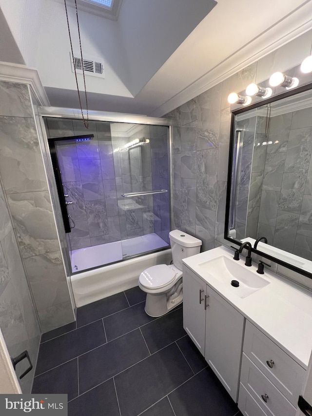 full bathroom featuring toilet, vanity, tile walls, tile patterned floors, and enclosed tub / shower combo