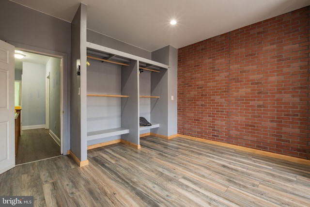 unfurnished bedroom with wood-type flooring, brick wall, and a closet