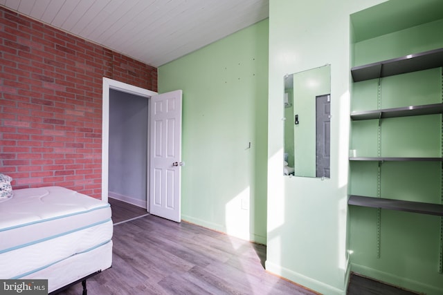 unfurnished bedroom with hardwood / wood-style flooring, electric panel, and brick wall