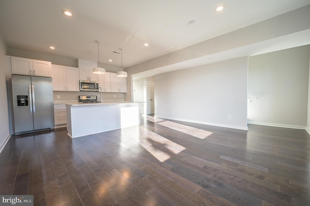 kitchen featuring stainless steel appliances, a kitchen island with sink, white cabinetry, and decorative light fixtures