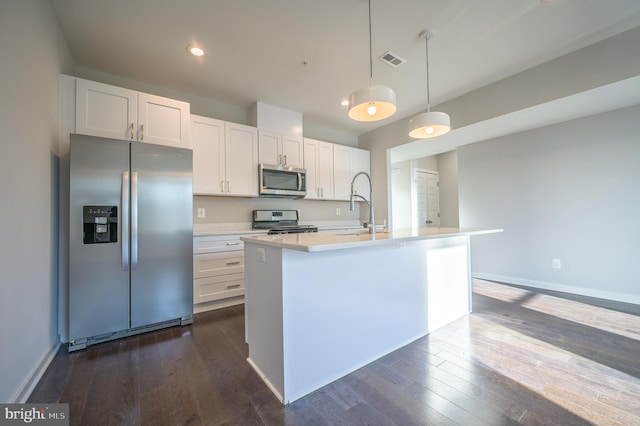 kitchen featuring decorative light fixtures, an island with sink, stainless steel appliances, and white cabinetry