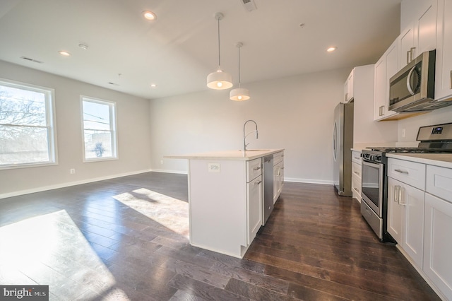 kitchen with appliances with stainless steel finishes, decorative light fixtures, white cabinetry, an island with sink, and sink