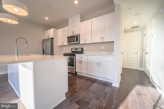 kitchen with an island with sink, appliances with stainless steel finishes, dark hardwood / wood-style flooring, white cabinets, and sink