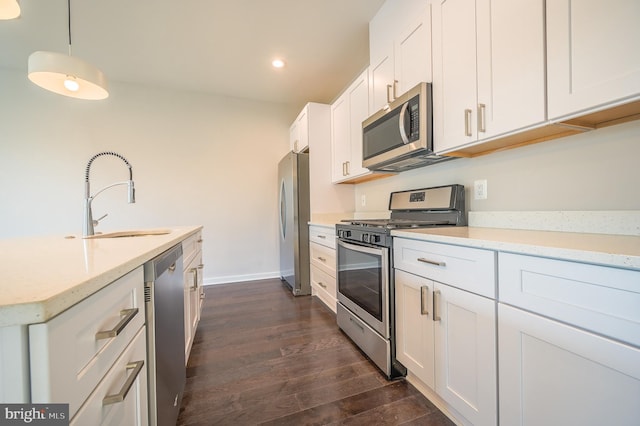 kitchen featuring white cabinets, appliances with stainless steel finishes, dark hardwood / wood-style flooring, sink, and hanging light fixtures