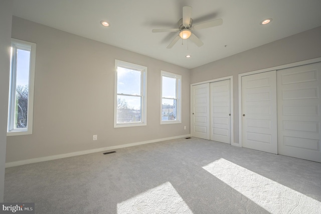 unfurnished bedroom featuring ceiling fan, light colored carpet, and two closets