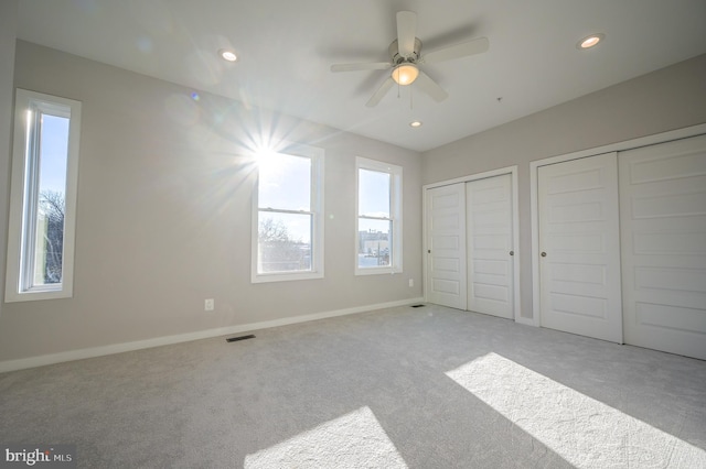 unfurnished bedroom featuring ceiling fan, light colored carpet, and multiple closets