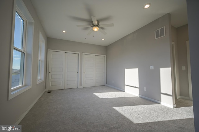 unfurnished bedroom with light carpet, multiple closets, and ceiling fan