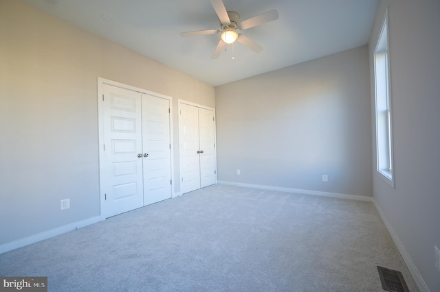 unfurnished bedroom with multiple closets, carpet flooring, and ceiling fan