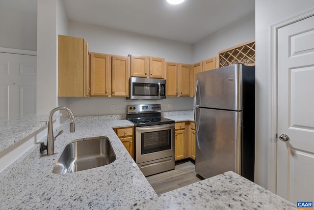 kitchen with light hardwood / wood-style floors, kitchen peninsula, sink, light stone countertops, and appliances with stainless steel finishes