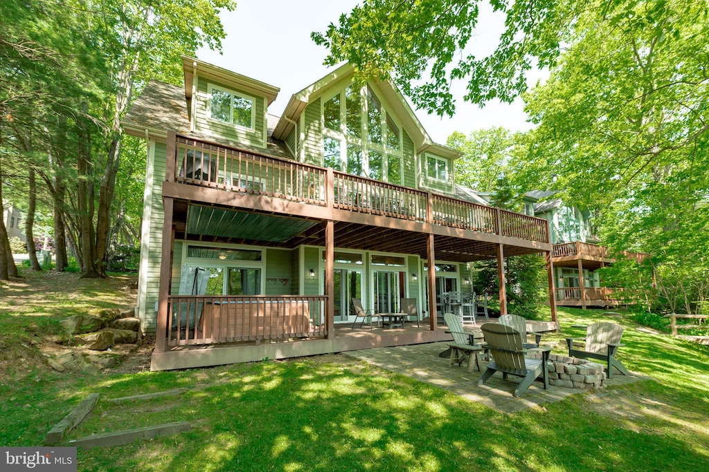 rear view of house featuring a wooden deck, a patio area, a lawn, and an outdoor fire pit