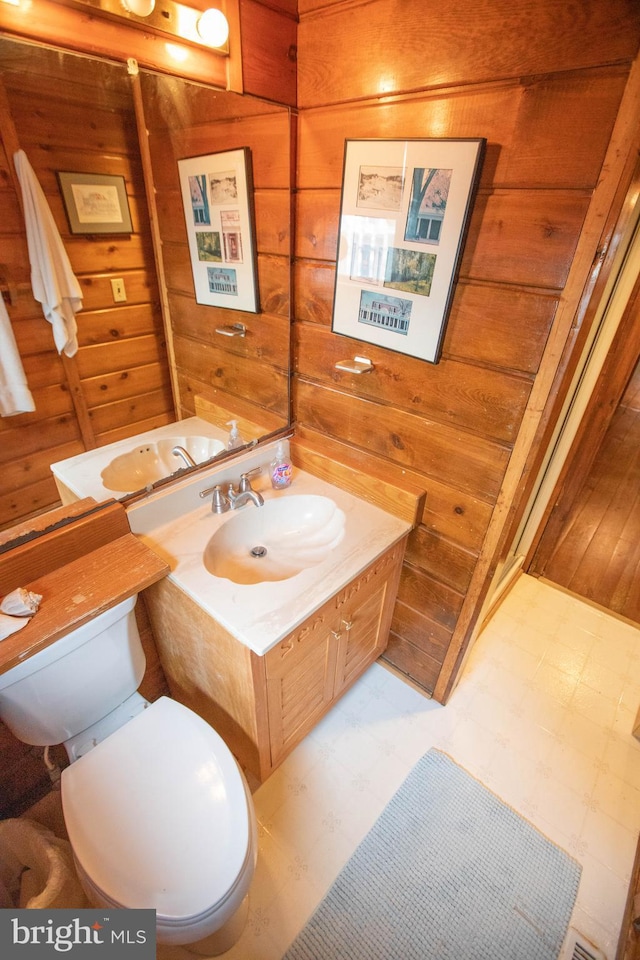 bathroom featuring toilet, vanity, and wooden walls