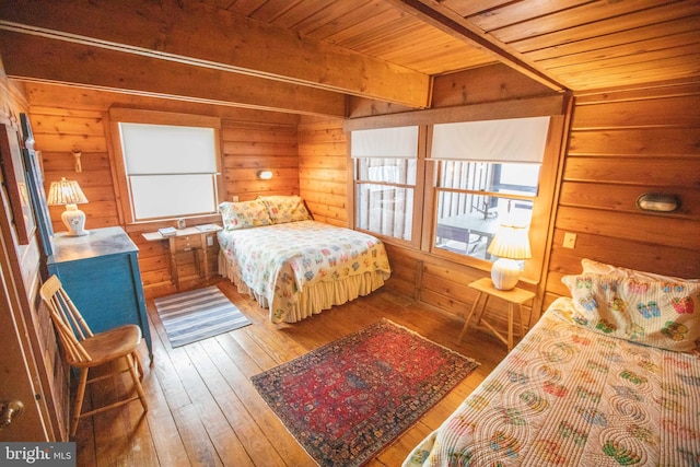 bedroom featuring multiple windows, beam ceiling, and wood walls