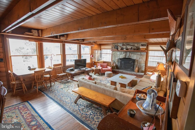 living room with beam ceiling, wood-type flooring, wooden ceiling, and a stone fireplace