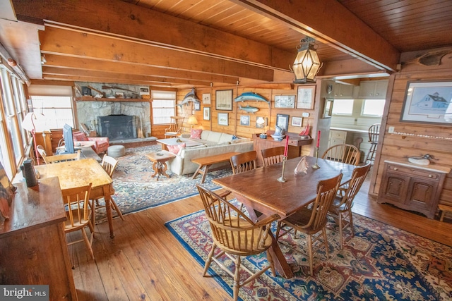 dining room featuring hardwood / wood-style flooring, a stone fireplace, wooden ceiling, and beam ceiling