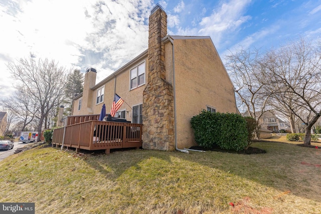 view of side of property with a yard, a chimney, a wooden deck, and stucco siding