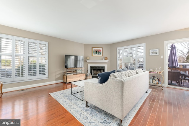 living area with a wealth of natural light, visible vents, a fireplace, and wood finished floors