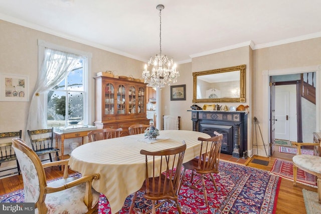 dining room featuring a fireplace, ornamental molding, a chandelier, and wood finished floors