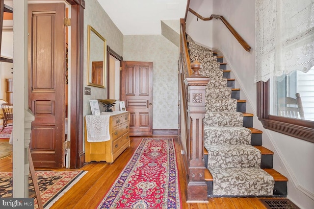 stairway featuring wallpapered walls, baseboards, visible vents, and hardwood / wood-style flooring