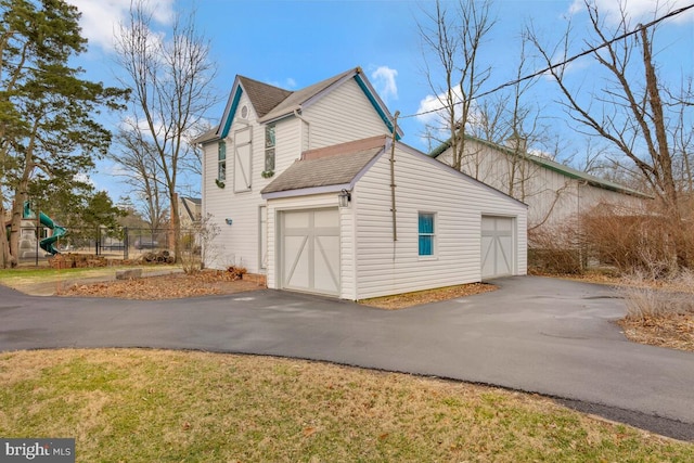 view of side of home with a garage, a shingled roof, fence, and a playground