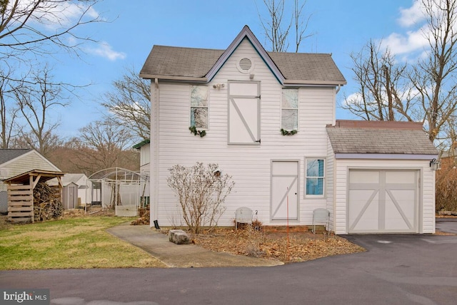 tudor house with driveway, an outbuilding, an attached garage, a storage unit, and a front lawn