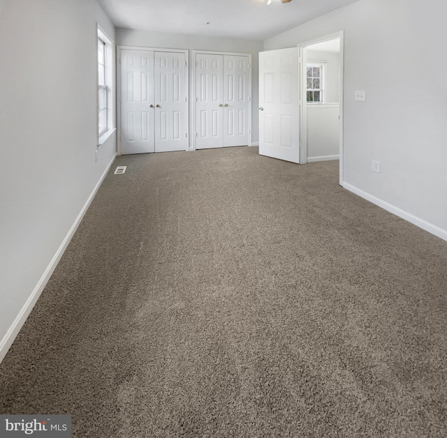 unfurnished bedroom featuring multiple closets and dark colored carpet