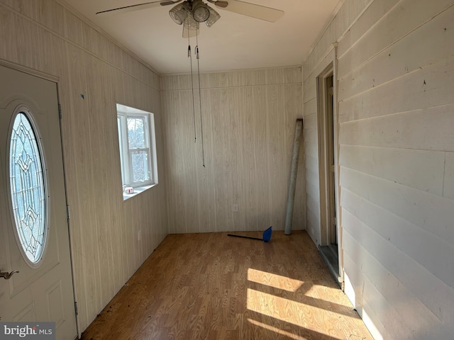 entryway featuring ornamental molding, wood walls, ceiling fan, and light wood-type flooring