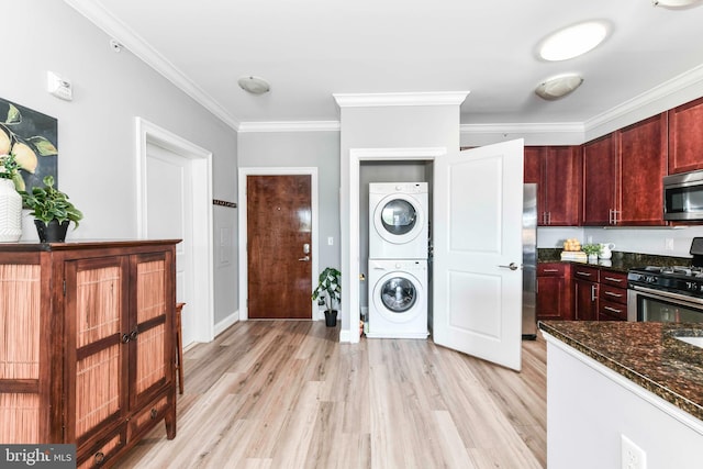 kitchen with stainless steel appliances, stacked washer and dryer, dark stone countertops, light wood-type flooring, and crown molding