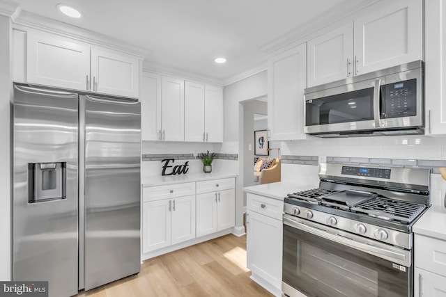 kitchen with white cabinetry, stainless steel appliances, tasteful backsplash, crown molding, and light hardwood / wood-style flooring