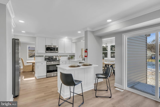 kitchen with kitchen peninsula, light wood-type flooring, a kitchen breakfast bar, stainless steel appliances, and white cabinets