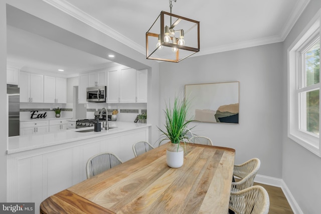 dining area with sink, wood-type flooring, crown molding, and an inviting chandelier