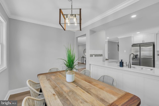 dining space featuring wood-type flooring, a notable chandelier, sink, and crown molding