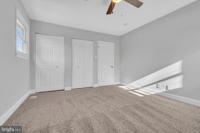 unfurnished bedroom featuring ceiling fan, two closets, and carpet flooring