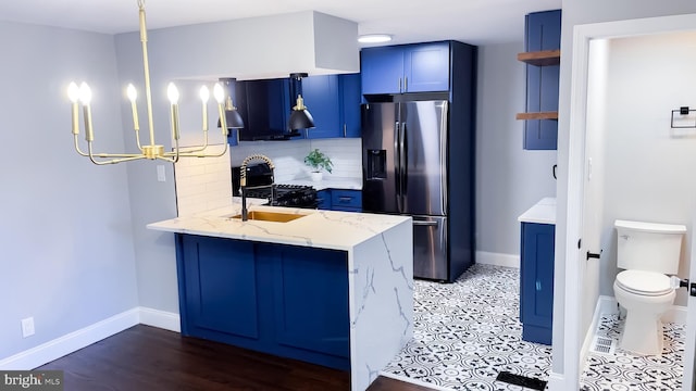 kitchen with stainless steel refrigerator with ice dispenser, decorative backsplash, kitchen peninsula, light stone counters, and blue cabinets