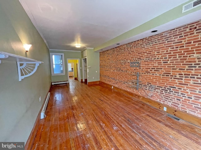 unfurnished living room with hardwood / wood-style flooring, brick wall, a baseboard heating unit, and crown molding