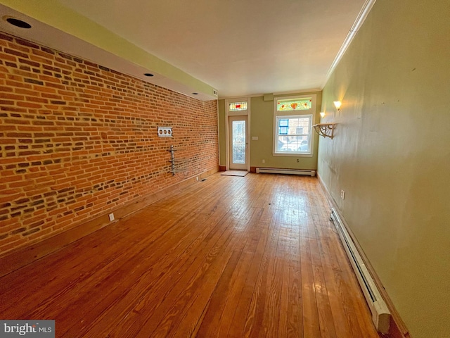 unfurnished living room featuring crown molding, light hardwood / wood-style floors, brick wall, and a baseboard heating unit