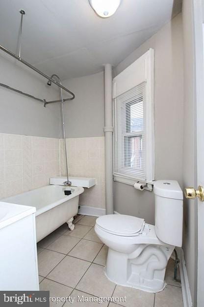 bathroom with toilet, tile walls, tile patterned flooring, a washtub, and vanity