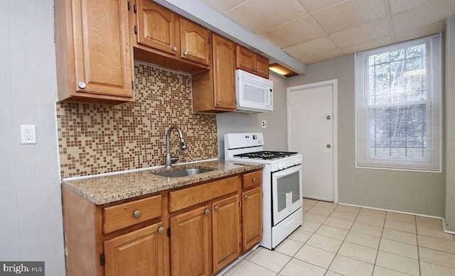 kitchen with white appliances, a drop ceiling, sink, backsplash, and light stone counters