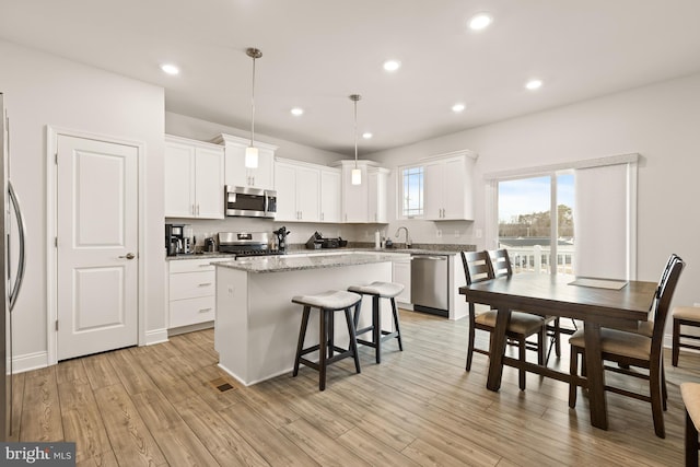 kitchen with a kitchen island, decorative light fixtures, white cabinetry, stainless steel appliances, and light hardwood / wood-style floors