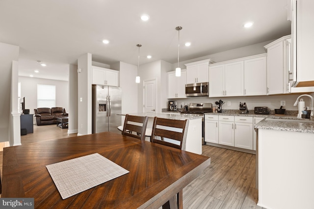 kitchen featuring appliances with stainless steel finishes, white cabinets, decorative light fixtures, sink, and light stone counters