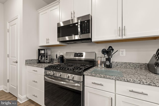 kitchen with hardwood / wood-style flooring, light stone countertops, white cabinetry, and stainless steel appliances