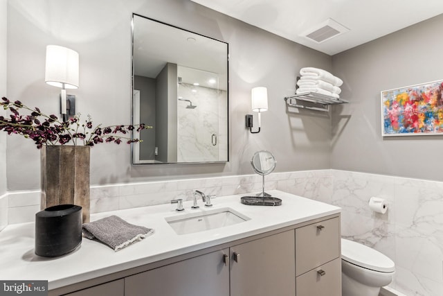 bathroom with vanity, a shower with shower door, tile walls, and toilet