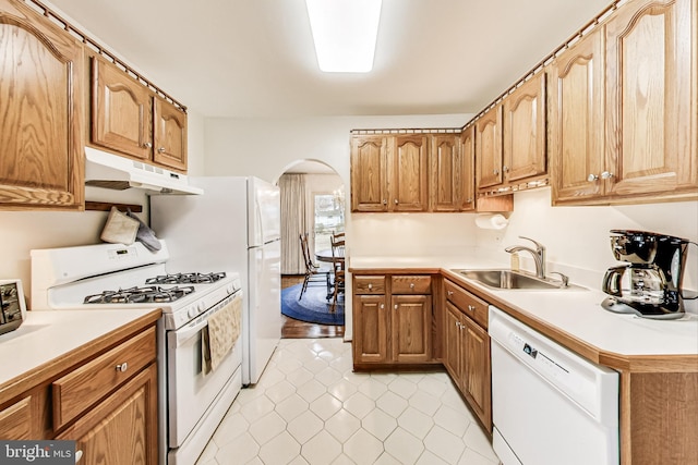 kitchen featuring white appliances, arched walkways, light countertops, under cabinet range hood, and a sink