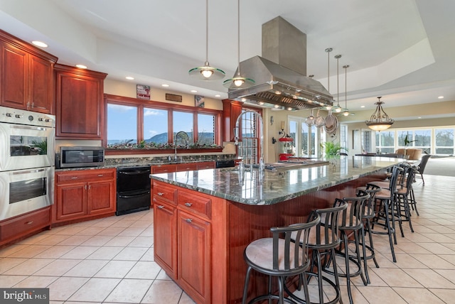 kitchen featuring dark stone countertops, hanging light fixtures, stainless steel appliances, island range hood, and a kitchen island