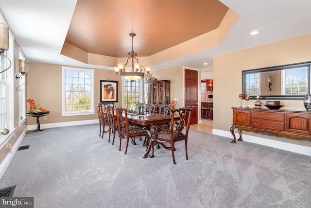 carpeted dining area featuring a raised ceiling and a chandelier